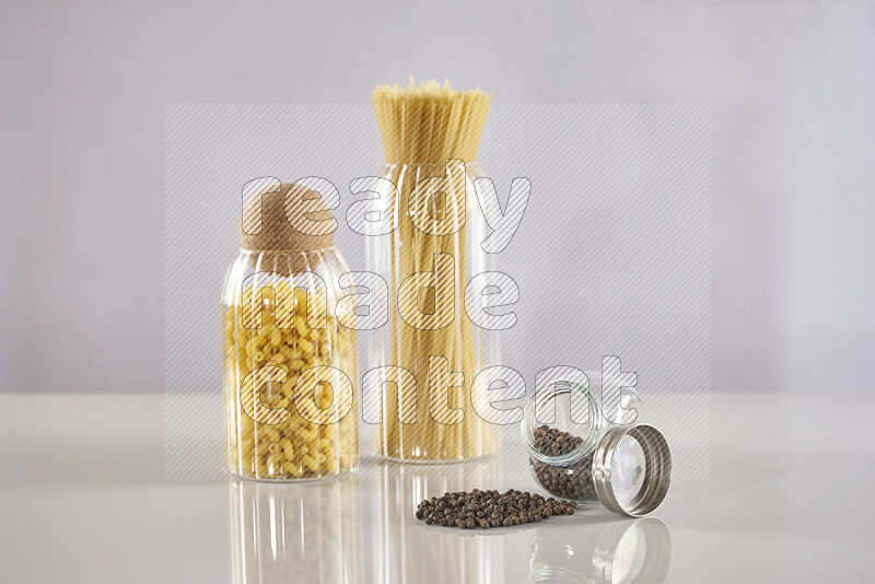 Raw pasta in glass jars with black peppers on light grey background