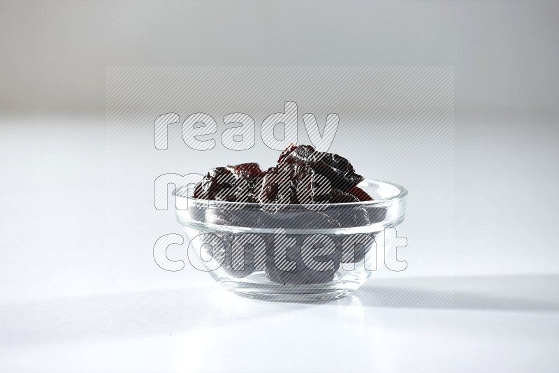 A glass bowl full of dried plums on a white background in different angles