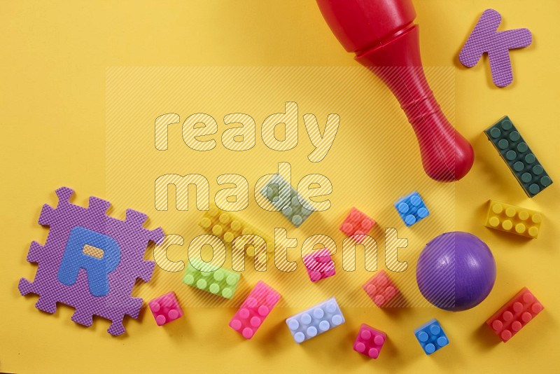 Plastic building blocks, balls and bowling pins on yellow background in top view (kids toys)