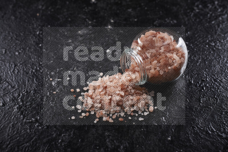 A glass jar full of coarse himalayan salt crystals on black background