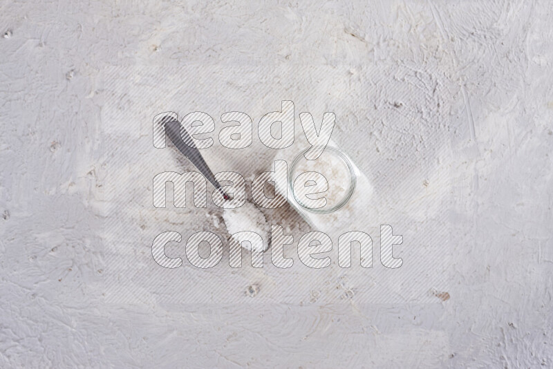 A glass jar full of coarse sea salt crystals on white background