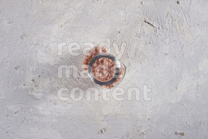 A glass jar full of coarse himalayan salt crystals on white background