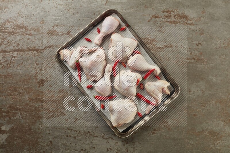 Mixed fresh chicken pieces in an oven tray on a textured rustic background