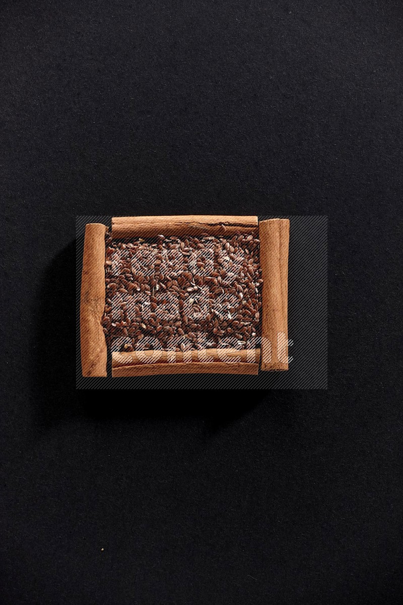 A single square of cinnamon sticks full of flaxseeds on black flooring