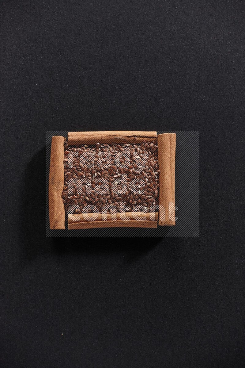 A single square of cinnamon sticks full of flaxseeds on black flooring