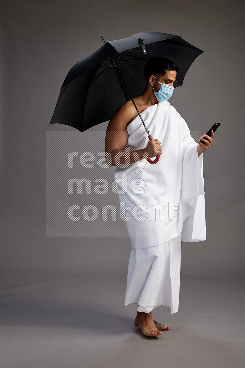 A man wearing Ehram and mask Standing holding umbrella on gray background on gray background