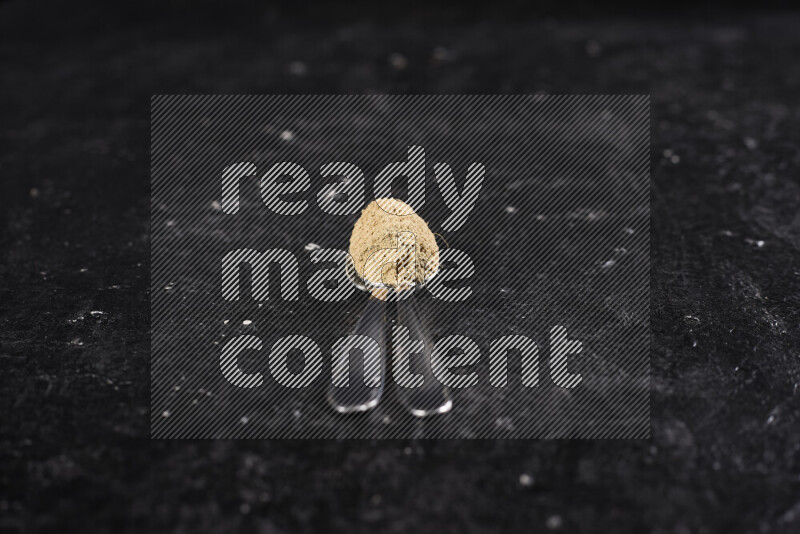 Two metal spoons full of ground ginger powder on black background