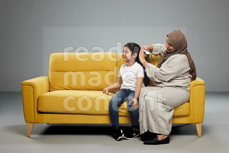 A mother sitting styling hair for her daughter on gray background