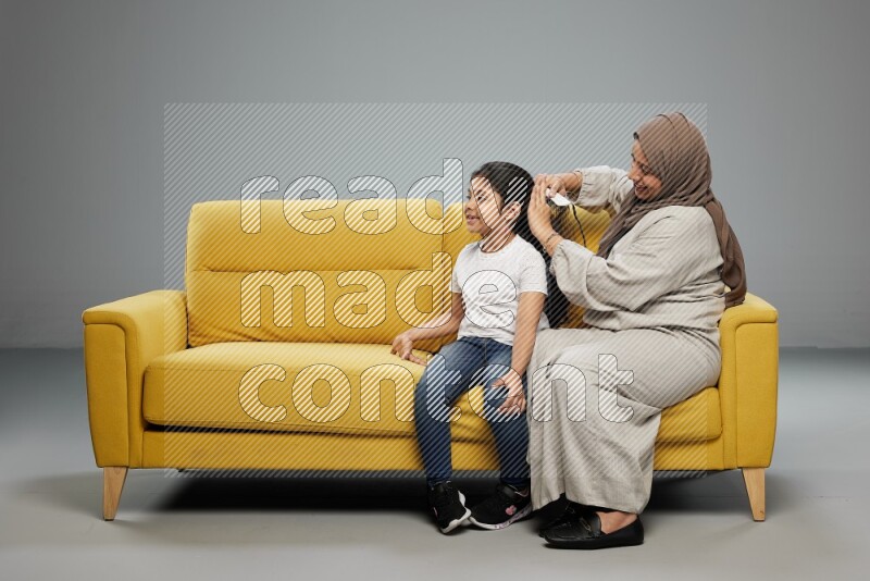 A mother sitting styling hair for her daughter on gray background