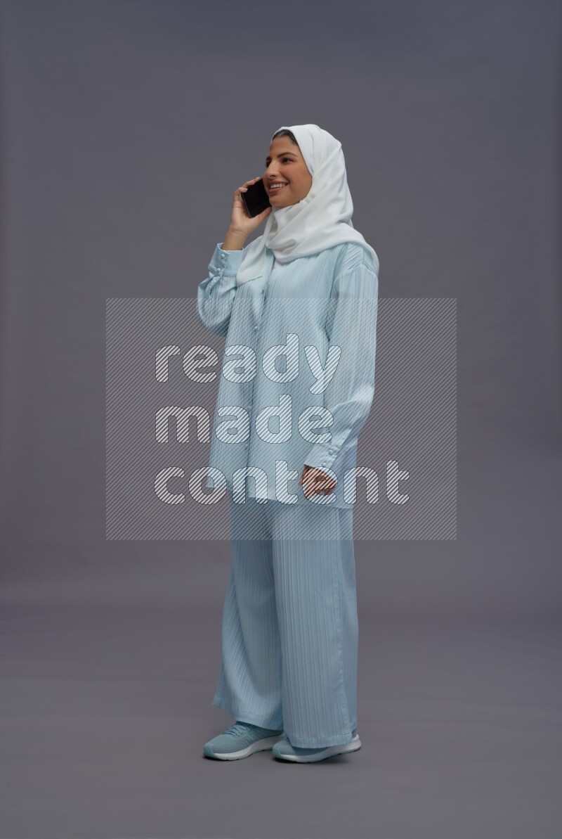 Saudi woman wearing hijab clothes standing talking on phone on gray background