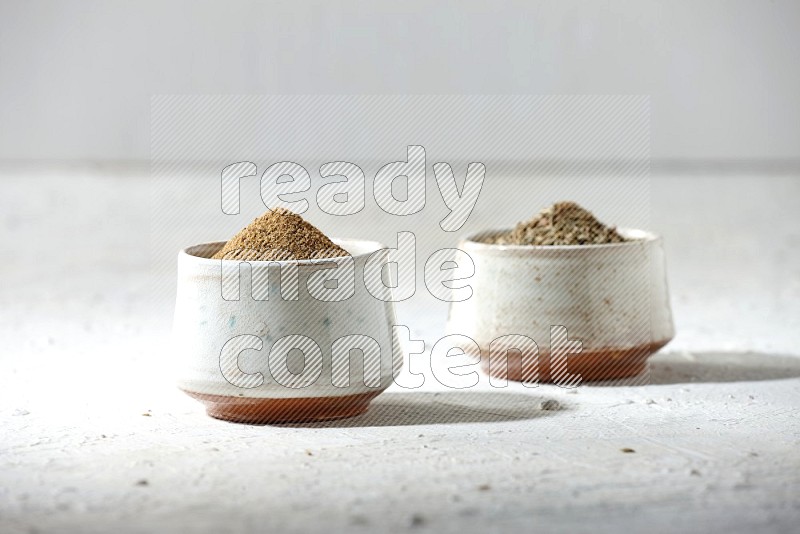 2 beige bowls full of cumin seeds and powder on a textured white flooring