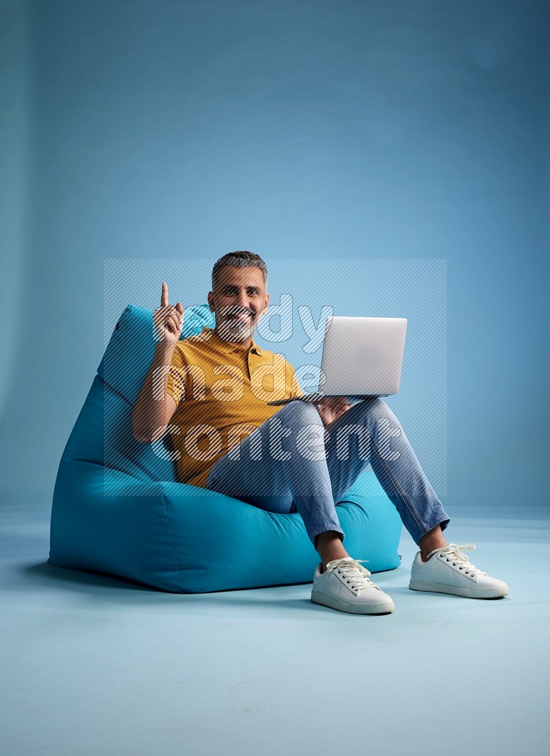 A man sitting on a blue beanbag and working on laptop