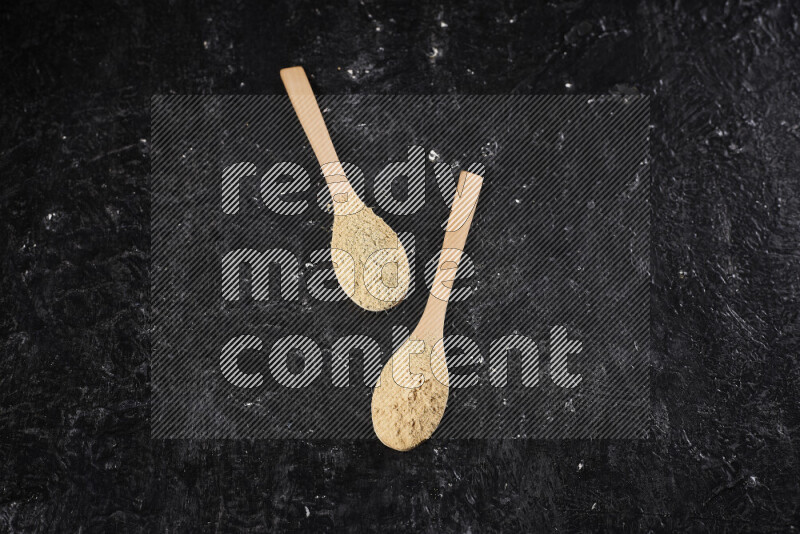 Two wooden spoons full of ground ginger powder on black background