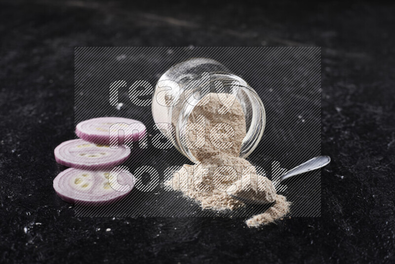 A glass jar full of onion powder flipped with some spilling powder on black background