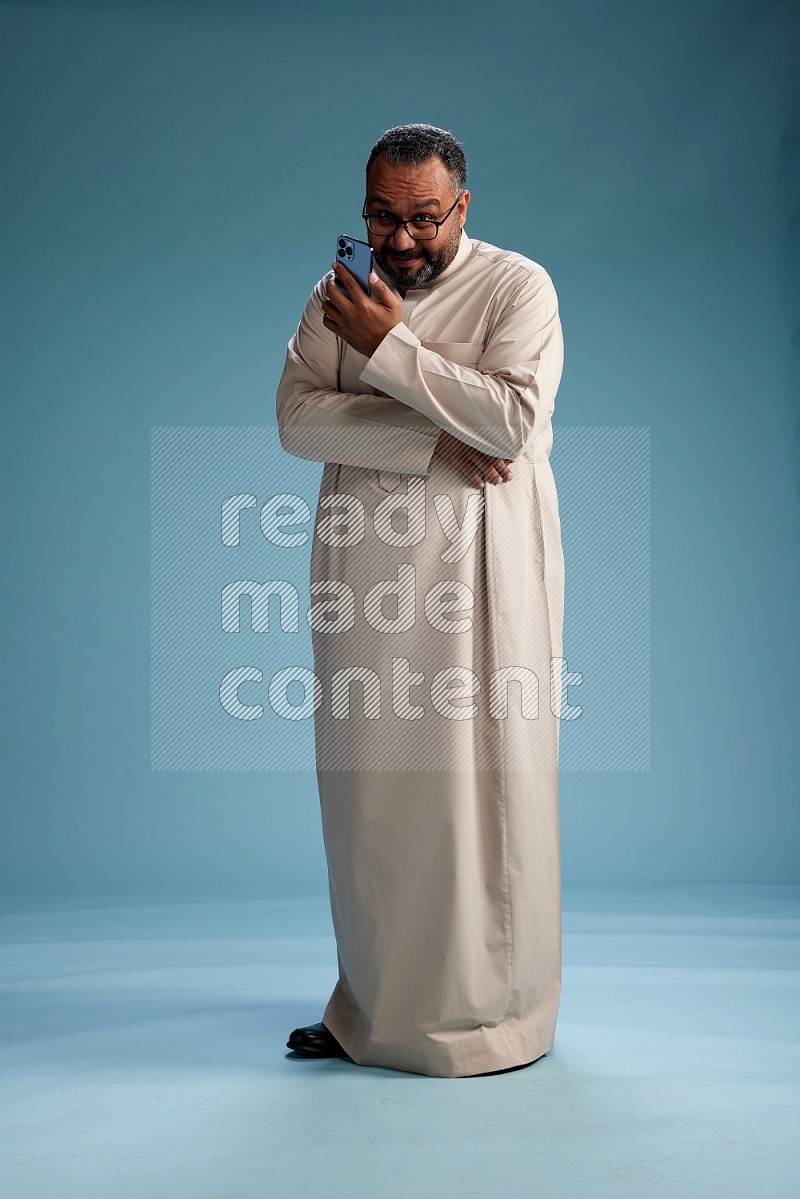Saudi Man without shimag Standing texting on phone on blue background