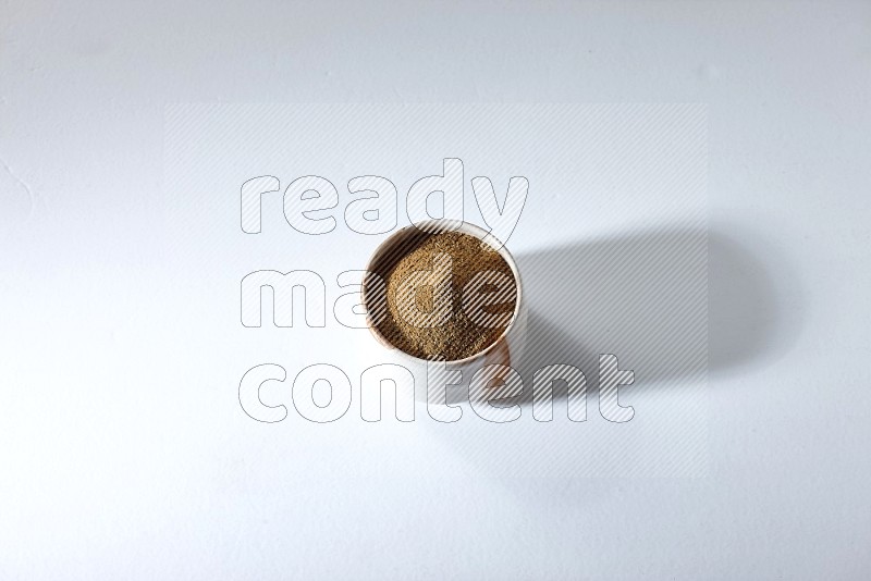 A beige bowl full of cumin powder on a white flooring