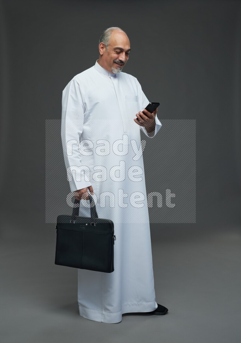 Saudi man without shomag Standing holding bag and phone on gray background