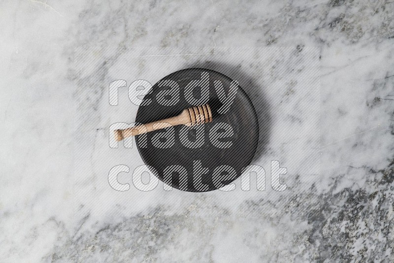 Black Pottery Plate with wooden honey handle in it, on grey marble flooring, Top View