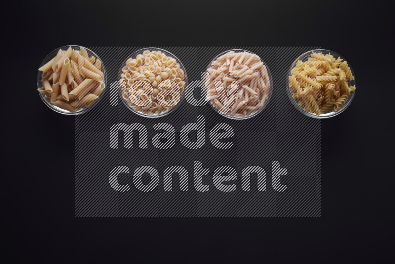 Different pasta types in glass bowls on black background