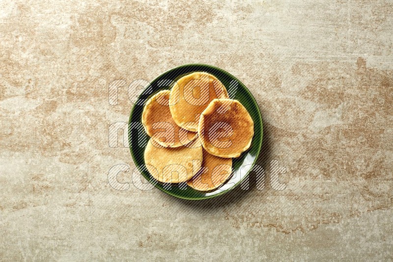 Five stacked plain mini pancakes in a green plate on beige background