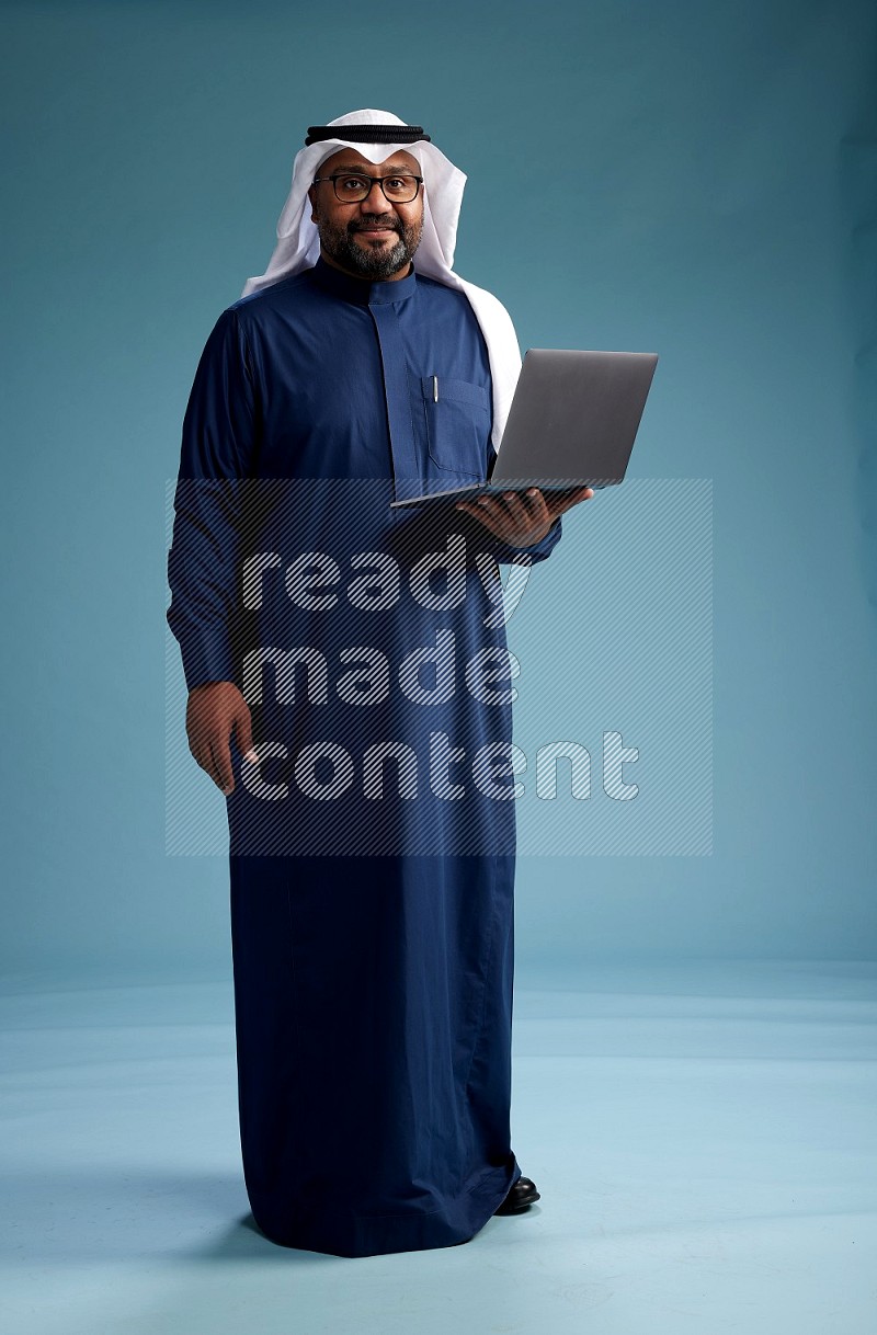 Saudi Man with shimag Standing working on laptop on blue background