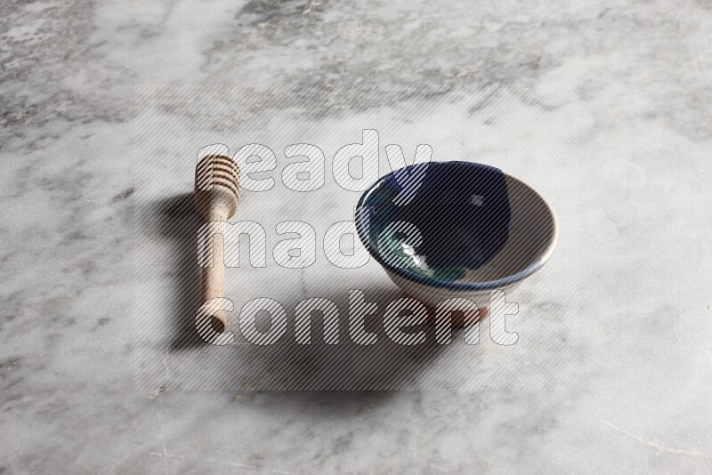 Multicolored pottery bowl with wooden honey dipper on the side on grey marble background
