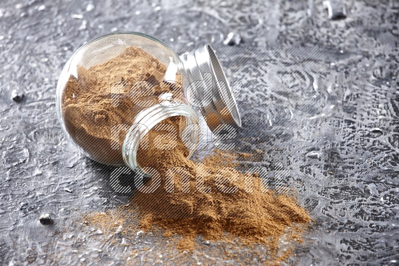 Flipped herbal glass jar full of cinnamon powder on textured black background