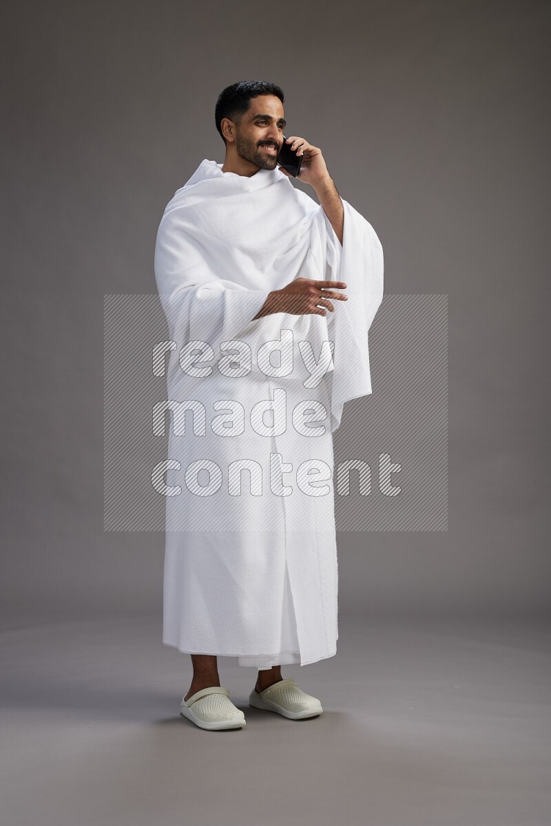 A man wearing Ehram Standing talking on phone on gray background