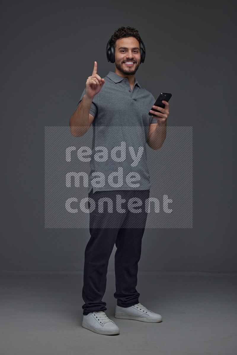 A man wearing casual and using his phone and headphone eye level on a gray background