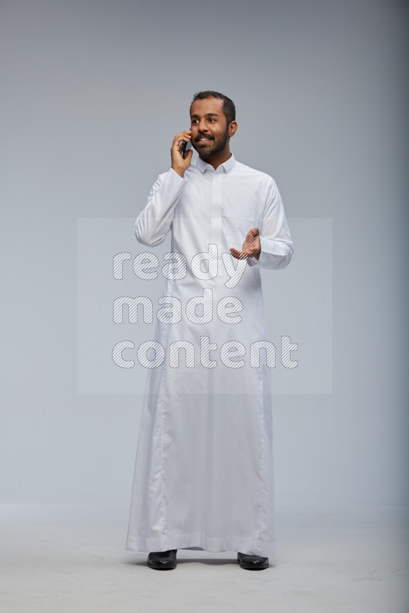 Saudi man wearing Thob standing talking on phone on Gray background