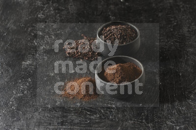 وعاءين من الفخار الأسود أحدهما ممتلئي بحبوب القرنفل والآخر ممتلئ ببودرة القرنفل على خلفية سوداء