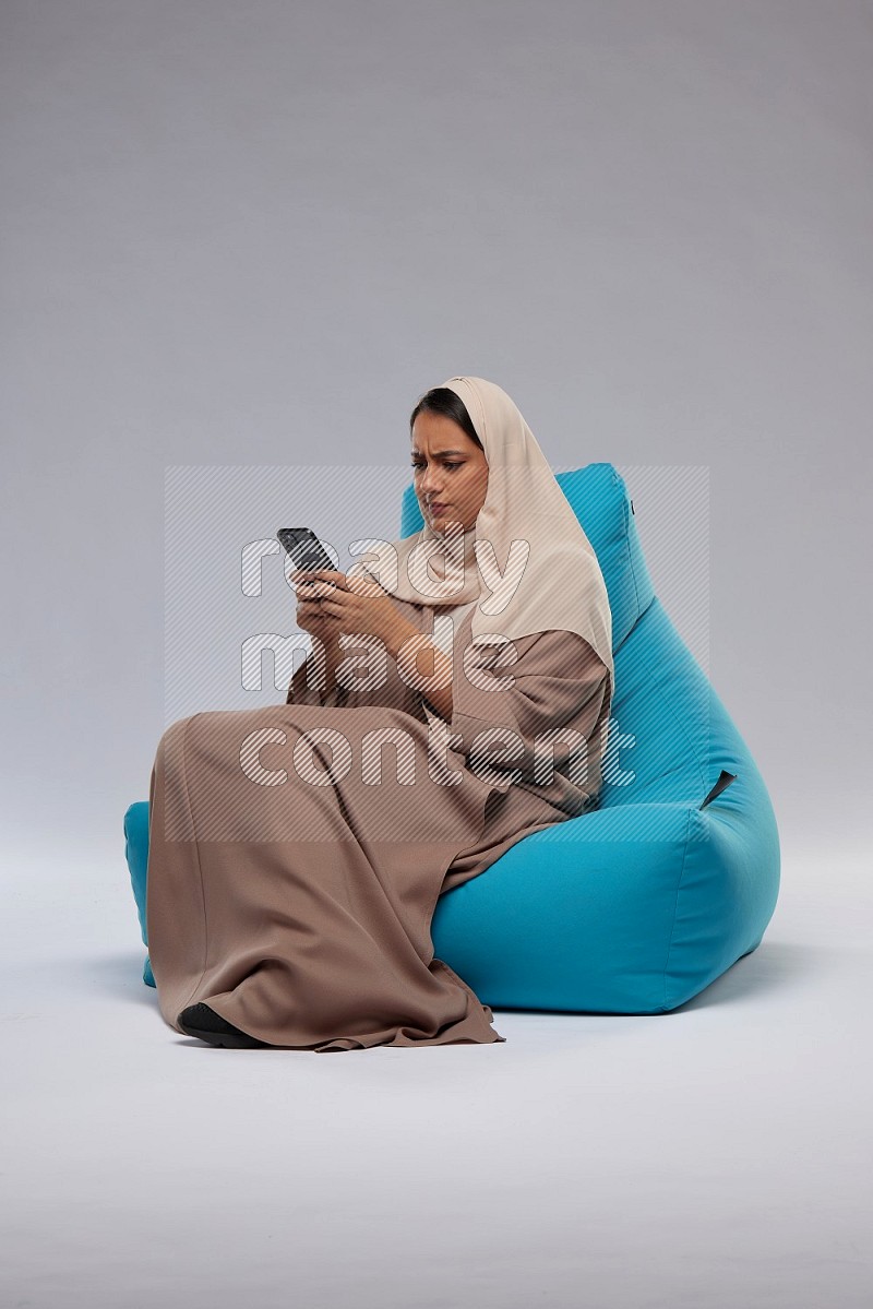 A Saudi woman sitting on a blue beanbag and texting on phone