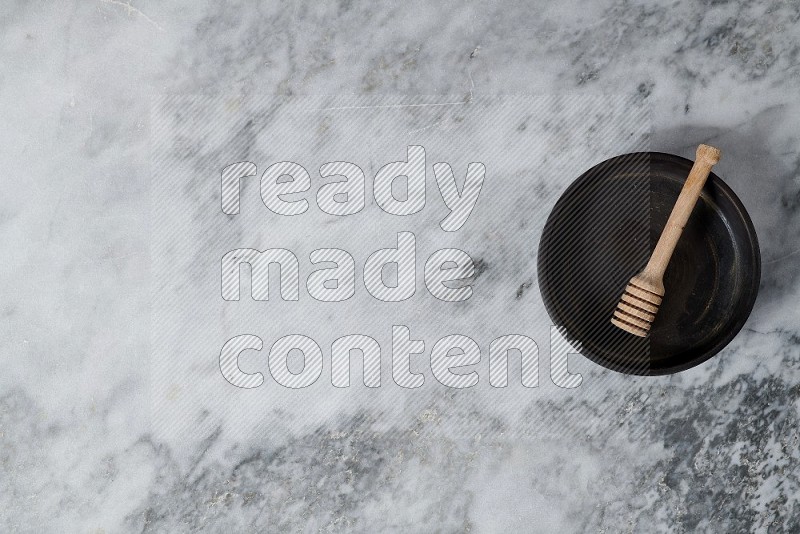 Black Pottery Oven Plate with wooden honey handle in it, on grey marble flooring, Top View