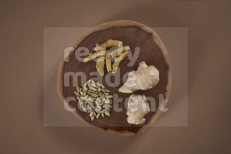 An assorted whole spices on a flat wooden tray including fresh and dried ginger, cinnamon sticks, cardamom, turmeric fingers, cloves, star anise on beige background