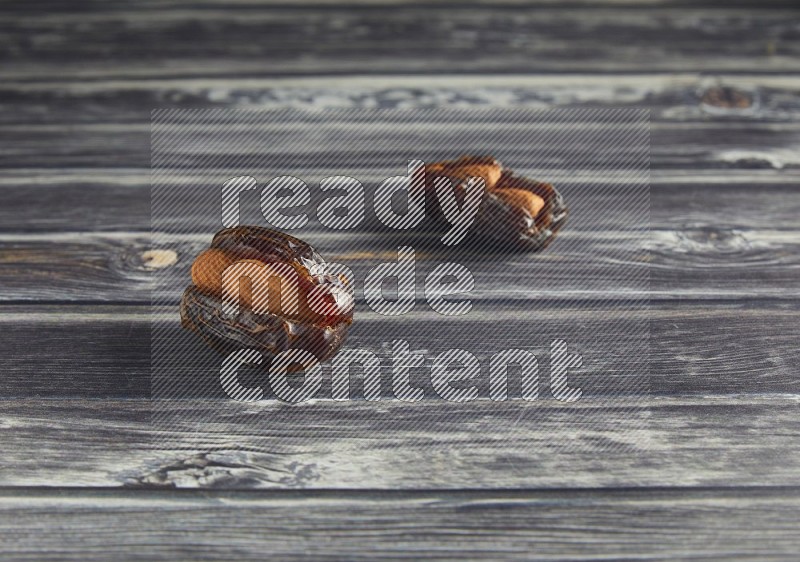 two almond stuffed madjoul dates on a wooden grey background