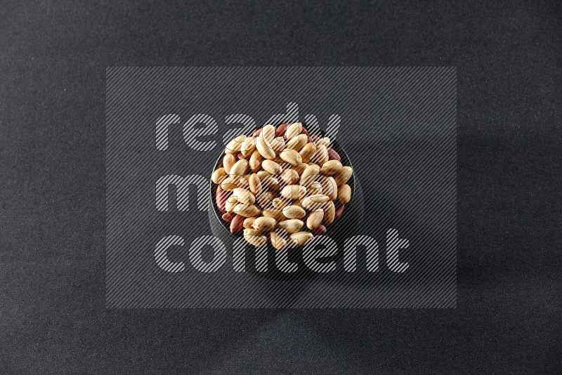 A black pottery bowl full of peeled peanuts on a black background in different angles