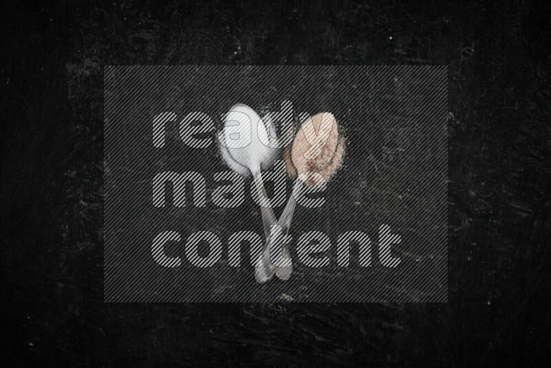 2 metal spoons filled with white salt and pink himalayan salt on black background