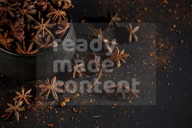 Star Anise in a black bowl with sprinkled anise on black flooring