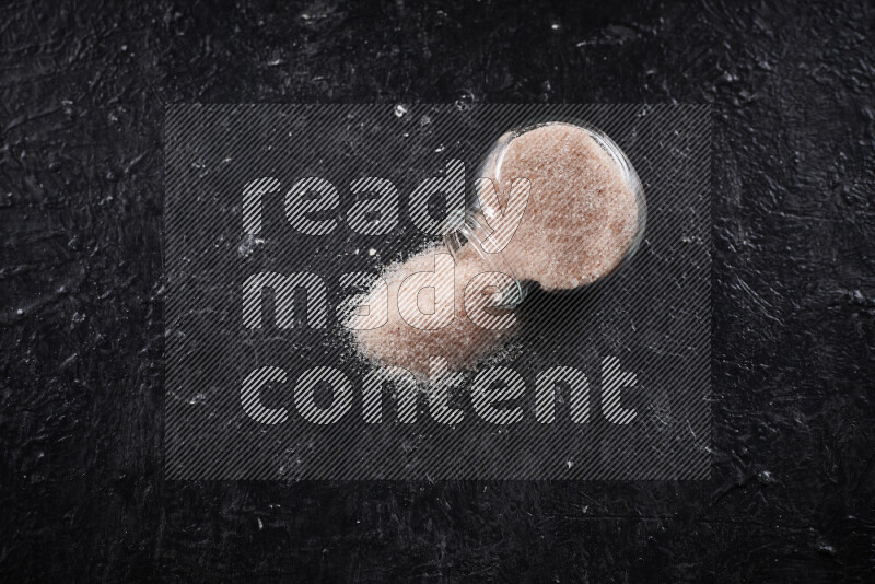 A glass jar full of fine himalayan salt on black background