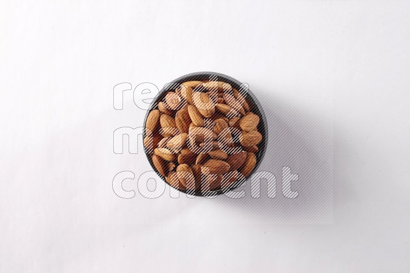 Almonds in a black pottery bowl on white background