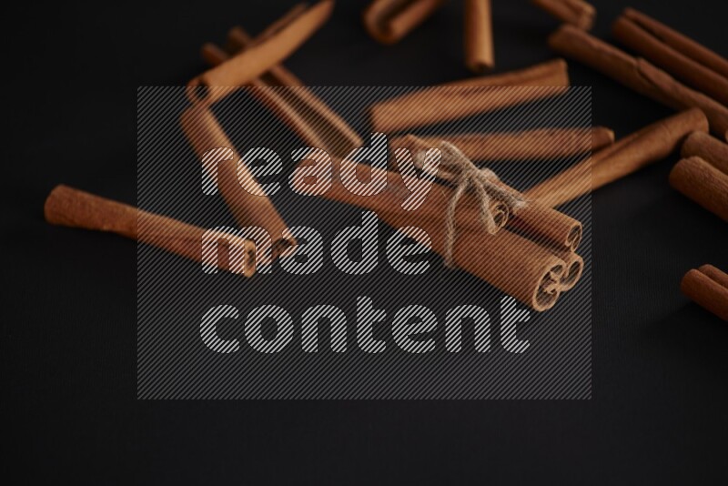 4 Cinnamon sticks stacked and bounded with more sticks in the background on black flooring