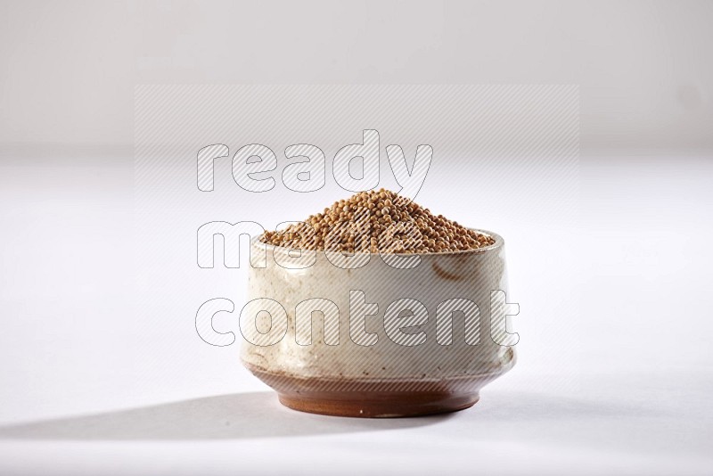 A beige pottery bowl full of mustard seeds on white flooring in different angles