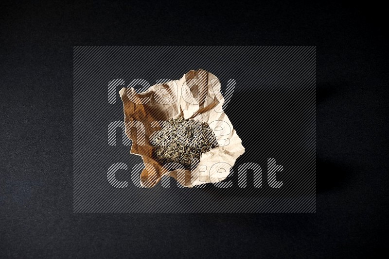 Cumin seeds in a crumpled piece of paper on black flooring