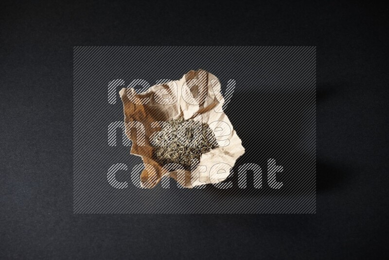 Cumin seeds in a crumpled piece of paper on black flooring