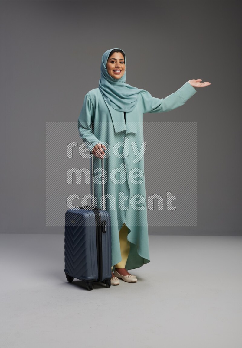 Saudi Woman wearing Abaya standing holding Travel bag on Gray background