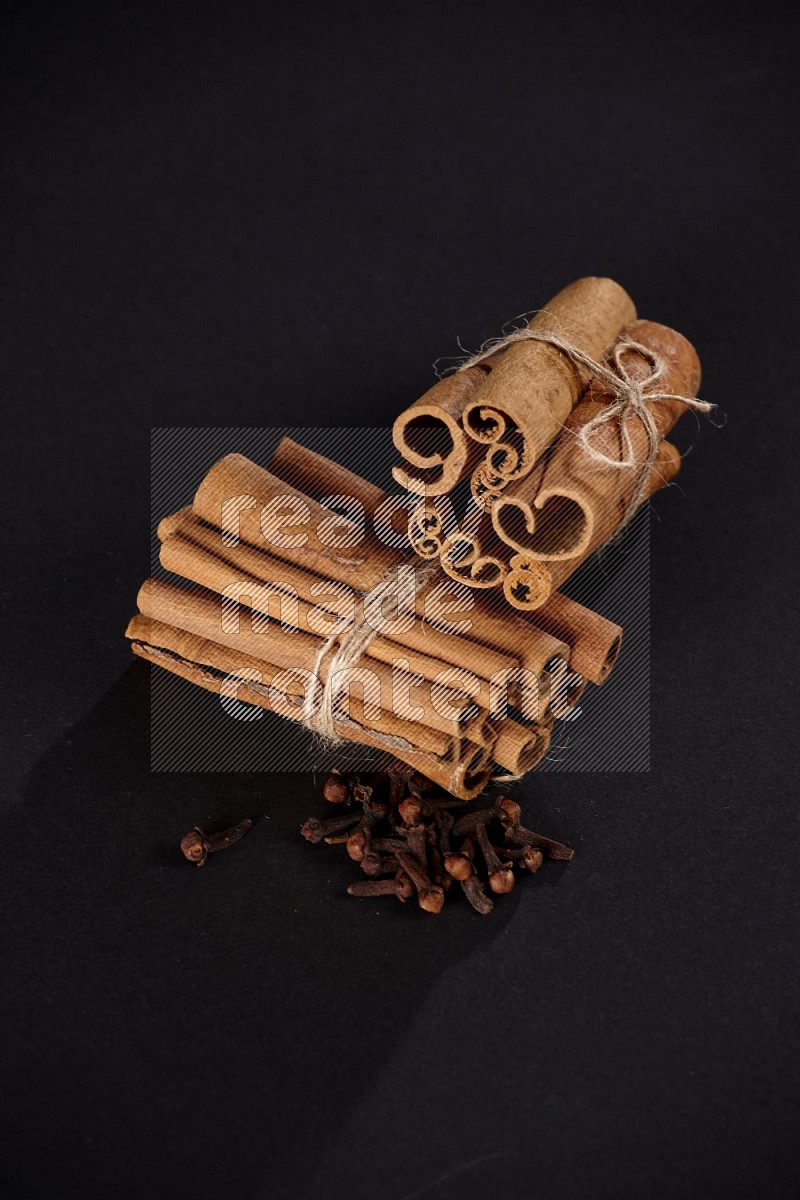 Two bounded stacks of cinnamon sticks with cloves on black background