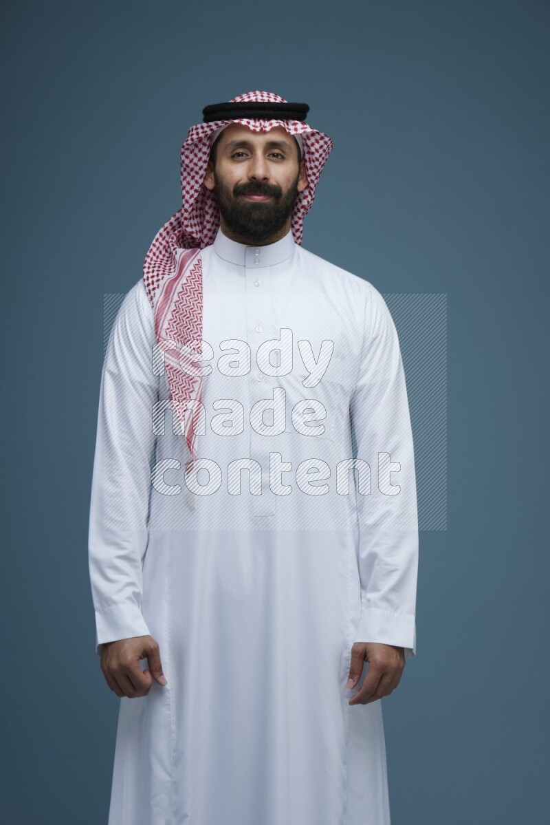 A man posing in a blue background wearing Saudi Thob and Shomag