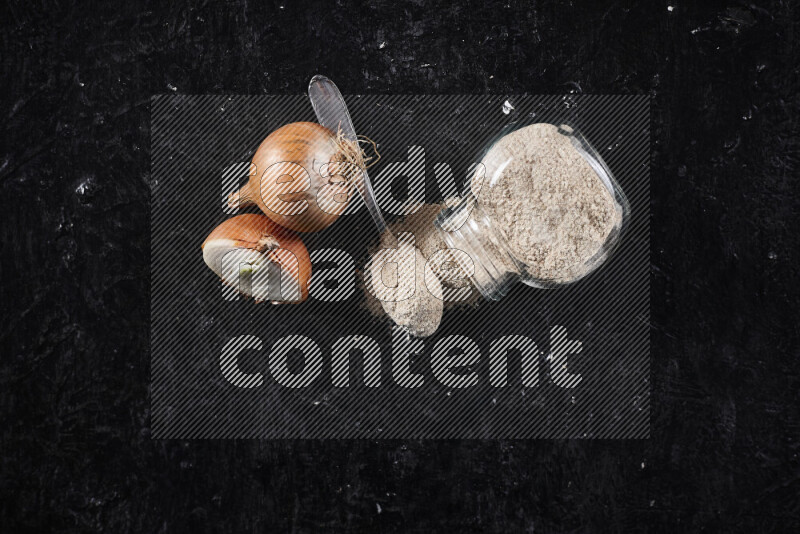 A glass jar full of onion powder flipped with some spilling powder on black background