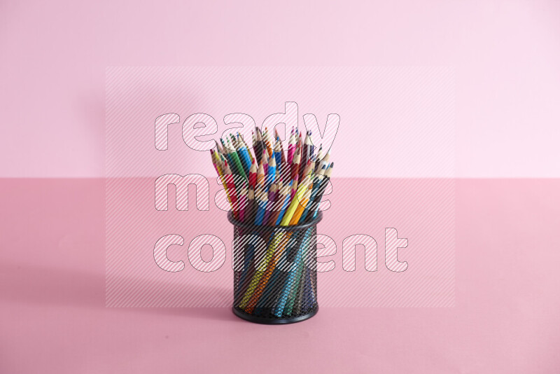 Pens, pencils and other different school supplies in a metal pen holder on rose background