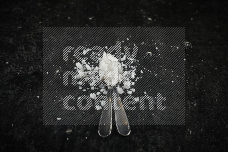 ملعقتان معدنيتان ممتلئتان بالملح الأبيض على خلفية سوداء